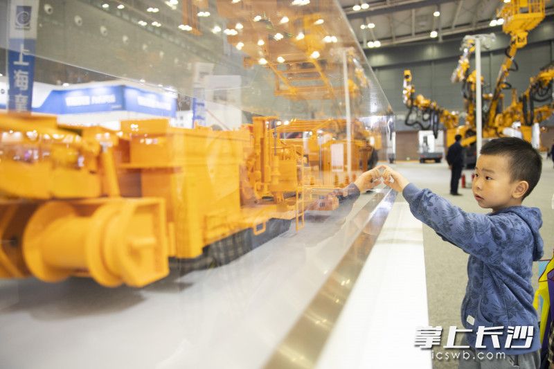 在鐵建重工展臺,，一位小朋友指著模型問家長,。