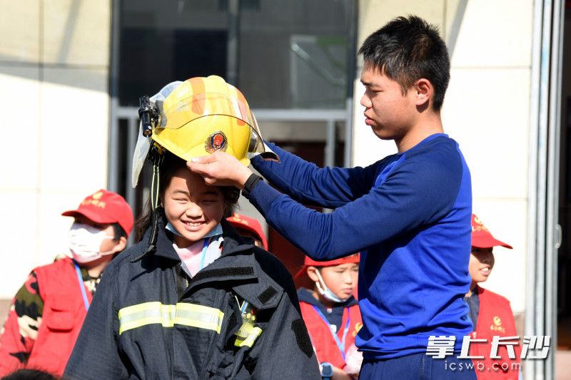 活動現(xiàn)場,，小記者體驗穿滅火防護服,，消防員為其戴上消防頭盔。