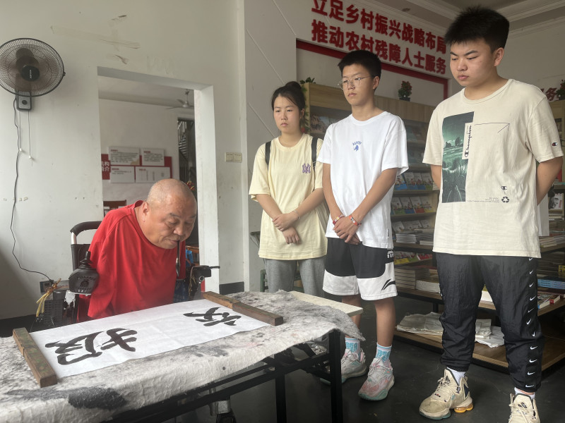 “半截人”周國民用嘴叼筆,，給兩位“準(zhǔn)大學(xué)生”（右一、右三）寫下“報效祖國”的青春寄語,。  均為長沙晚報全媒體記者 黎鐵橋 攝