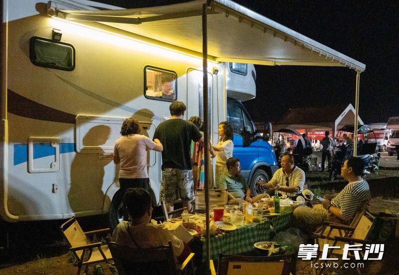 游客們愜意的坐在房車下，吹著晚風(fēng),，品嘗美食,。
