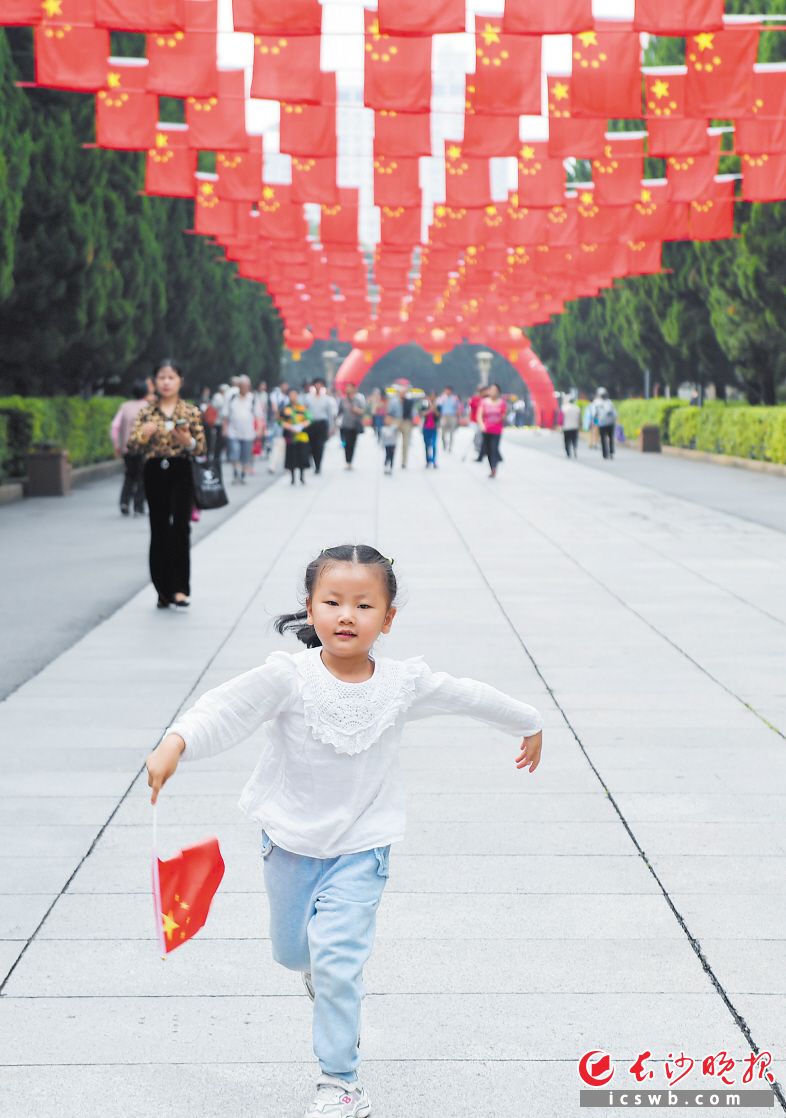 10月1日，烈士公園南門紅旗招展,，一個小朋友手持小國旗自由奔跑,，感受美好的節(jié)日時光。